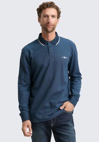 Langärmliges navy Polohemd mit weißem Kragenrand, Knopfleiste und Logo-Detail auf der Brust. Der Stoff wirkt leicht und hat eine strukturierte Oberfläche.