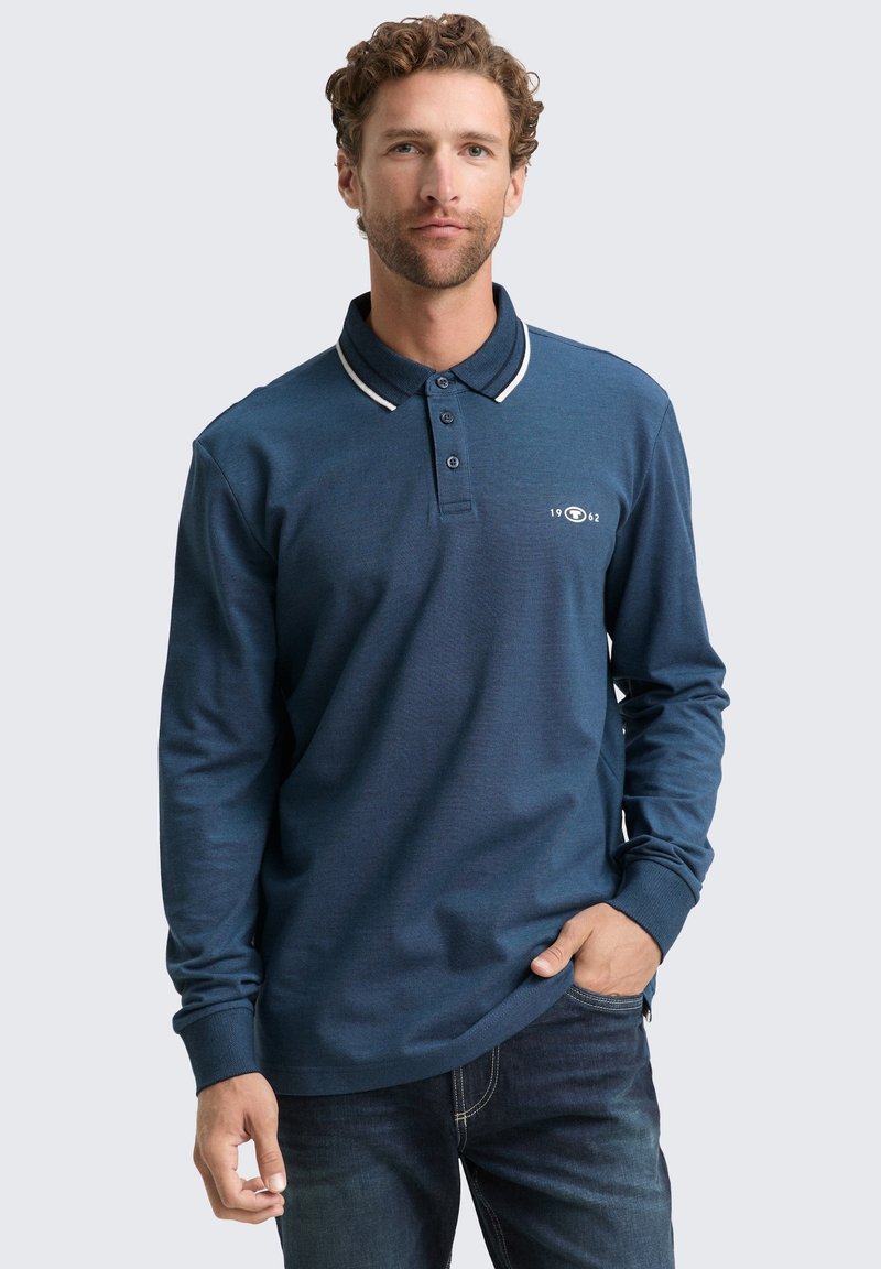 Langärmliges navy Polohemd mit weißem Kragenrand, Knopfleiste und Logo-Detail auf der Brust. Der Stoff wirkt leicht und hat eine strukturierte Oberfläche.