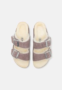 Lichtpaarse suede sandalen met twee verstelbare zilverkleurige gespsluitingen en een zachte, crèmekleurige shearling voering. Plat zoolontwerp.