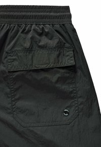 Schwarze technische Shorts mit einem elastischen Bund, einer Gesäßtasche mit Klappe und einem runden Logo-Akzent auf der unteren rechten Seite.