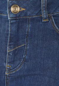 Jeans i denim med en djupt blå färg, med gul sömnad, en framträdande framficka och en metallknappsstängning.