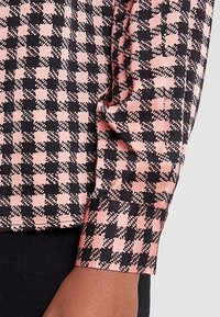 Rosa och svart rutmönstrad blus i ett mjukt material, med långa ärmar och manschettdetalj, som framhäver en slät textur och mönster.