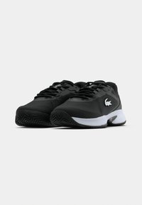 Czarne buty sportowe z teksturowaną cholewką, wiązaniem na sznurówki, białą podeszwą środkową i charakterystycznym logo. Posiadają gumową podeszwę zewnętrzną o zygzakowatym wzorze.