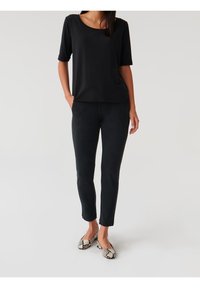 Sort kortærmet top i en afslappet pasform; sorte skræddersyede bukser med sidesømme; mønstrede ballerinaer med et slange-design. Glat stof og minimalistisk stil.