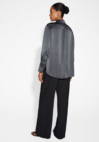 Camicia grigia in satin con bottoni, orlo arrotondato e maniche lunghe, abbinata a pantaloni neri a gamba larga. Tessuto liscio e vestibilità comoda.