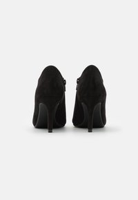 Chaussures à talons hauts en daim noir avec un design à bout pointu et un détail zippé sur les côtés, dotées d'un talon aiguille élégant.