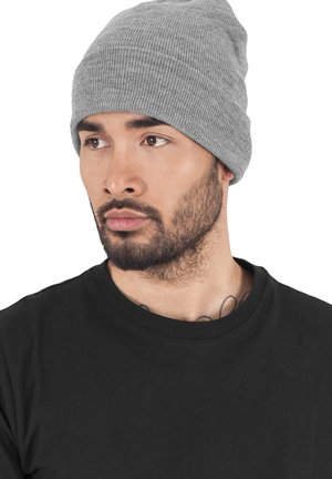 Gray knit beanie with a ribbed texture, rolled cuff, and soft material. Worn by a male model in a black t-shirt, showcasing versatility.