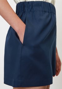 Námořnické modré kraťasy s elastickým pasem, které mají postranní kapsy a hladký povrch, navržené pro pohodlí a snadný pohyb.