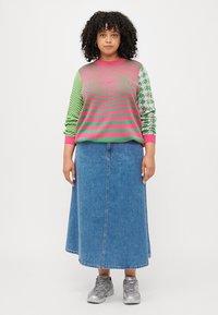 Multicolor knitted sweater with green, pink, and striped patterns; paired with a long denim skirt and metallic sneakers.