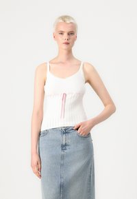 Vit ribbad tank top med ömtålig spetskant och rosa dragsko i midjan, kombinerad med en ljusblå denimkjol.