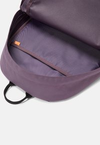 Lila ryggsäck interiör med en slät yta, med ett randigt foder och en orange etikett. Inkluderar en fack för organisering.