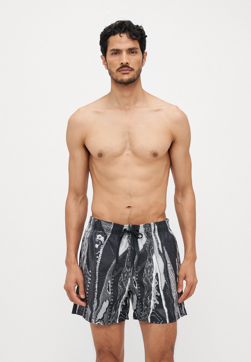 Shorts de bain noirs et blancs pour homme avec un motif ondulé, taille élastique et cordon de serrage. Tissu léger avec une coupe décontractée.