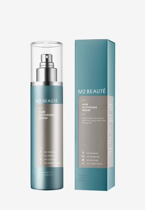 Haaraktivierungsserum in einer zylindrischen Glasflasche mit einem silbernen Pumpkopf, präsentiert in einer blauen und silbernen Schachtel mit Produktinformationen und ohne Symbolik.