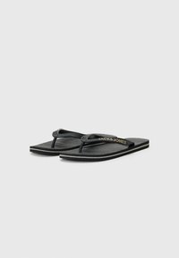 Sorte flip-flops med tekstureret fodseng og let hævede kanter. Har gummistropper med brandlogo i guld på én strop.