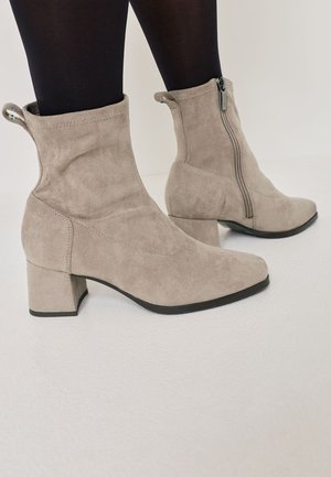 Beige suede ankle boots with a square toe, block heel, and side zipper. Features a folded cuff and smooth texture.