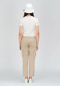 Beige cargobyxor med sidfickor, kombinerade med en vit kort t-shirt och en vit bucket hat. Enkel design med en avslappnad passform.