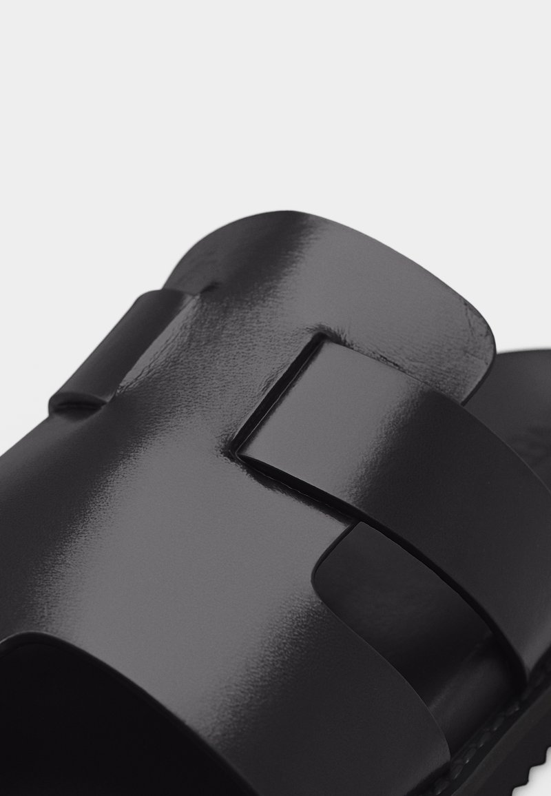 Close-up of black glossy slide sandal with wide strap featuring rectangular cutout detail.