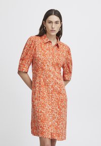 Abito a maniche corte con bottoni di colore arancione e un motivo floreale. Realizzato in tessuto leggero, presenta una silhouette leggermente aderente e un colletto piatto.