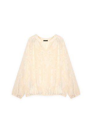 Blouse crème à manches longues, décolleté en V, ourlet élastique, et motif floral subtil sur tissu transparent. Finition texturée qui renforce l'intérêt visuel.