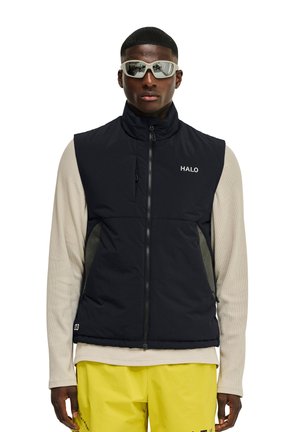 Sort polstret vest med lynlås, høj krave og "HALO"-logo. Udstyret med sidede paneler i net, båret over en lys langærmet top, kombineret med gule bukser.