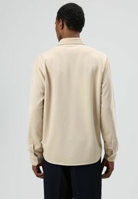 Beige langarmshirt met een zachte textuur, voorzien van een klassieke kraag en met knopen sluitbare manchetten. Glad stof valt zacht en benadrukt de silhouet.