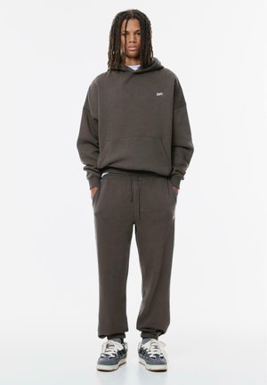 Mørkegrå sweatshirt og matchende sweatpants lavet af en bomuldsblanding. Hooded design med en frontlomme og elastiske manchetter. Sneakers med hvide snørebånd.