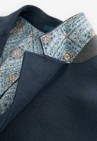 Dunkelblaues Blazer aus strukturiertem Stoff mit einem bunten Innenfutter im Paisleymuster. Auffälliges Kragen design mit kontrastierenden Elementen.