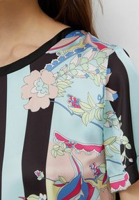 Blusa fluida con un motivo floreale in morbidi colori pastello su uno sfondo nero, con scollatura nera e maniche corte e larghe.