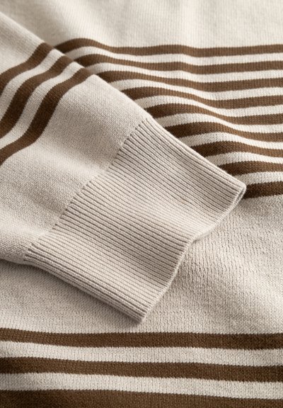 Pull en tricot beige clair avec des rayures horizontales marron, poignets côtelés et texture douce. Gros plan sur la zone de la manche.