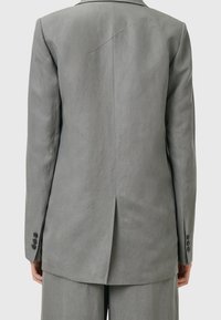 Grauer maßgeschneiderter Blazer mit langen Ärmeln, einer hinteren Schlitze, knöpfbaren Manschetten und glatter Textur. Auffälliges Nahtdetail auf der Rückseite.