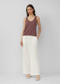 Lichte bordeaux geknoopte tanktop met een V-hals, gecombineerd met loszittende witte linnen broeken en beige sandalen met bandjes.