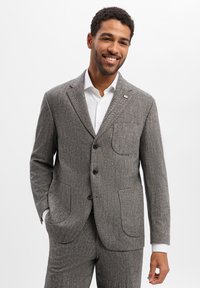 Szara marynarka w jodełkę z klapami z nacięciem, dwoma przednimi kieszeniami i trzema guzikami. W połączeniu z białą koszulą, podkreślająca dopasowany krój.