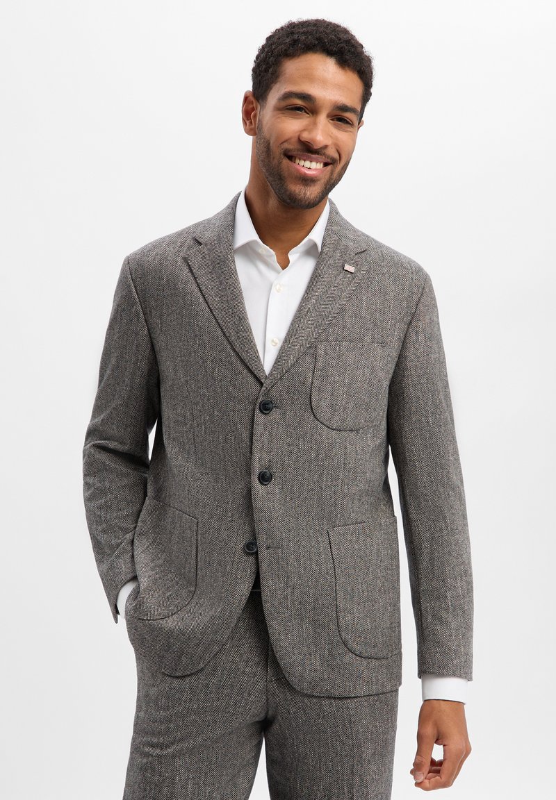 Szara marynarka w jodełkę z klapami z nacięciem, dwoma przednimi kieszeniami i trzema guzikami. W połączeniu z białą koszulą, podkreślająca dopasowany krój.