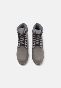 Cizme gri din suede cu șireturi negre, guler căptușit și material texturat. Talpa prezintă un design robust pentru tracțiune.
