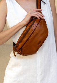 Brun läder crossbody-väska med rund form, dragkedjestängning och justerbar rem. Slät struktur med subtil detalj av varumärke.