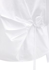 Biała bawełniana koszula z marszczonym materiałem po bokach, z cienkim detalem w postaci wiązania. Gładka textura z przeszyciem wokół krawędzi i listwy guzikowej.