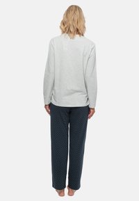 Grijze lange mouwen top gecombineerd met donkerblauwe pyjamabroek met stippen. De top heeft een relaxte pasvorm; de broek heeft een rechte snit en een zachte textuur.