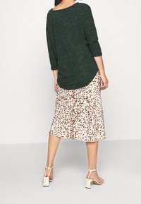 Vihreä teksturoitu neulepaita, jossa on kolmen neljänneksen hihat, yhdistettynä liehuvaan kermaan väriseen hameeseen, jossa on ruskeita leopardikuviota, sekä nilkkahihnaisiin korkokenkiin.