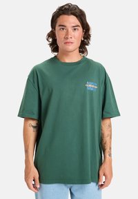Camiseta de algodón verde con mangas cortas, cuello redondo y un diseño gráfico en azul y naranja en la parte frontal. Ajuste casual.