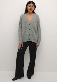 Cardigan grigio a maglia con scollatura a V, sei bottoni e taglio morbido. Abbinato a pantaloni neri a gamba larga e scarpe con tacco per un look completo.