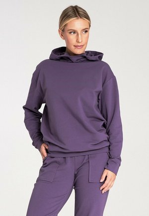 Fioletowy sweatshirt z kapturem, wykonany z miękkiego materiału, charakteryzujący się luźnym krojem i przednią kieszenią. W połączeniu z pasującymi fioletowymi spodniami.