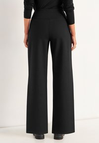 Schwarze, weit geschnittene Hose aus glattem Stoff mit hohem Bund und langen, fließenden Beinen, die ein schlichtes Design aufweist und keine sichtbaren Verschlüsse hat.