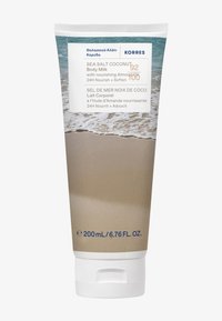 Tube blanc avec un socle en crème texturé, présentant une scène de plage et une marque. Contient 200 mL de lait corporel à la noix de coco et au sel marin. Capuchon scellé.