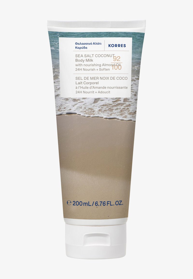 Tube blanc avec un socle en crème texturé, présentant une scène de plage et une marque. Contient 200 mL de lait corporel à la noix de coco et au sel marin. Capuchon scellé.
