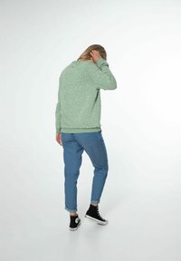 Sweat-shirt vert avec des taches blanches, coupe décontractée, poignets et ourlet côtelés. Associé à un pantalon en denim bleu clair retroussé et des baskets montantes noires.