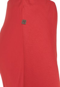 Indumento in tessuto leggero di colore rosso, presenta una superficie liscia e un piccolo logo metallico in risalto sulla cucitura laterale.