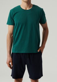 Zielona bawełniana koszulka z okrągłym dekoltem i krótkimi rękawami, w zestawie z ciemnonawigacyjnymi szortami z elastycznym paskiem ze sznurkiem.