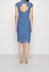 Niebieska koronkowa sukienka z krótkimi rękawkami, odsłoniętymi plecami, falbaniastym wykończeniem u dołu i zapięciem na suwak. Noszona z białymi sandałkami na obcasie.