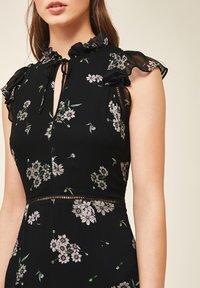 Svart klänning med blommönster, med en volangkrage, nyckelhålsöppning fram och en figurnära överdel. Texturerad tyg med delikata detaljer.