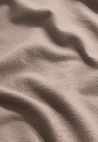 Tissu tricot beige avec une surface douce et texturée, affichant de douces vagues et plis, mettant en valeur son élasticité et sa flexibilité.